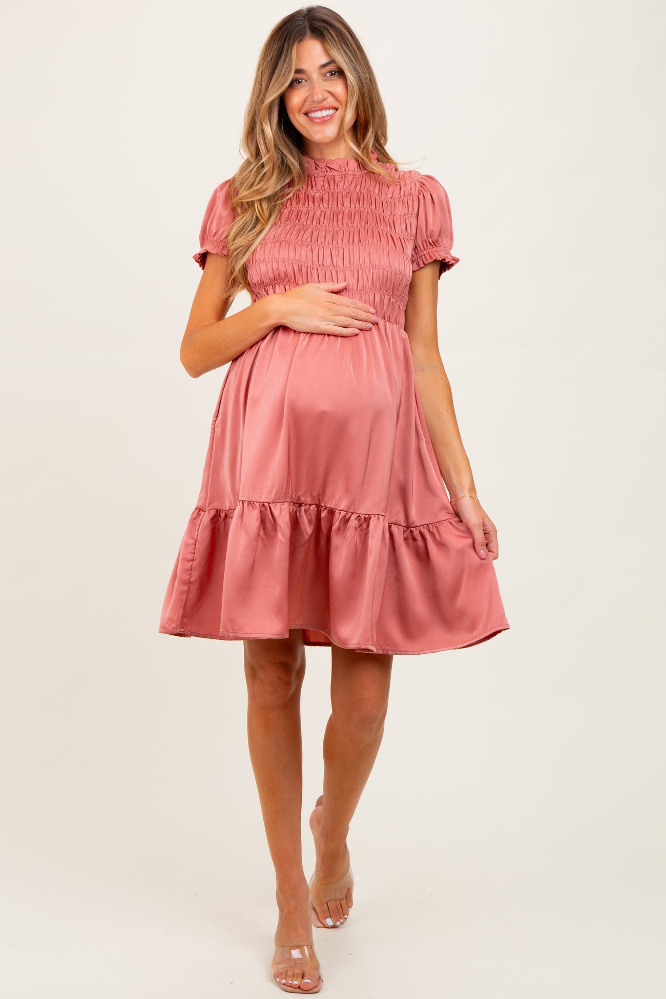 woman wearing a dusty rose maternity dress with smocked bodice and ruffled hem, holding her baby bump