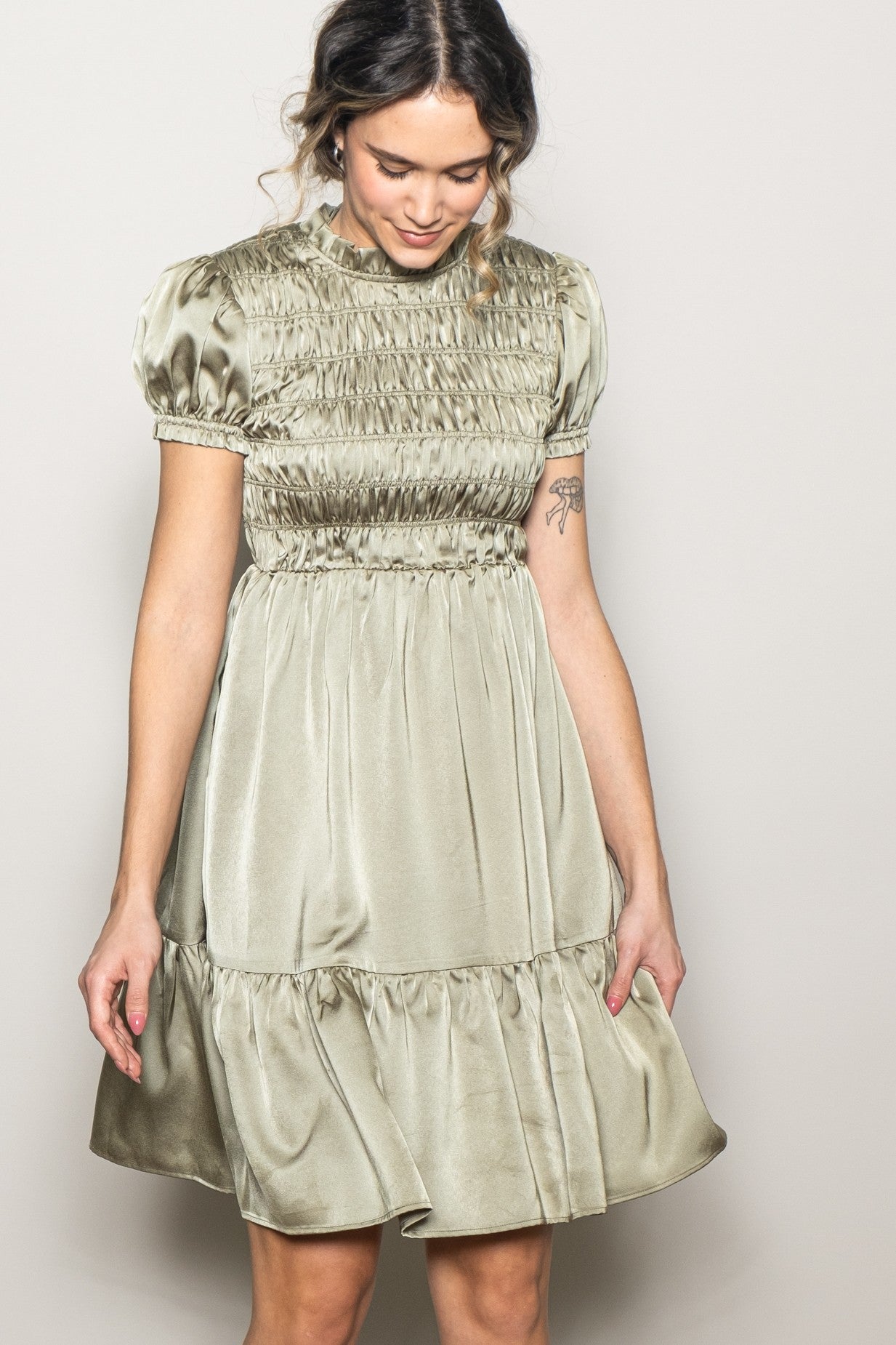 woman wearing an olive green smocked mini dress with puff sleeves and a tiered skirt
