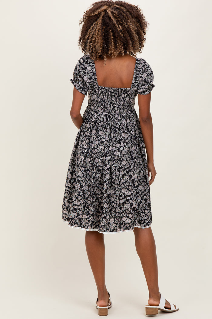 woman wearing a black floral maternity dress with short puff sleeves and a smocked back, showing her baby bump