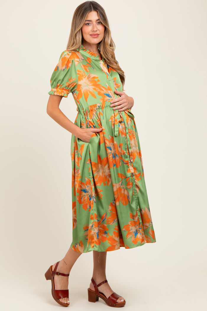 woman wearing a green floral maternity dress with short sleeves and a gathered waist, holding her baby bump