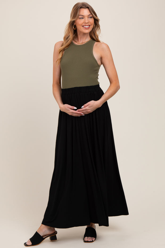 woman wearing a dark olive ribbed maternity tank top and a black maxi skirt, holding her baby bump