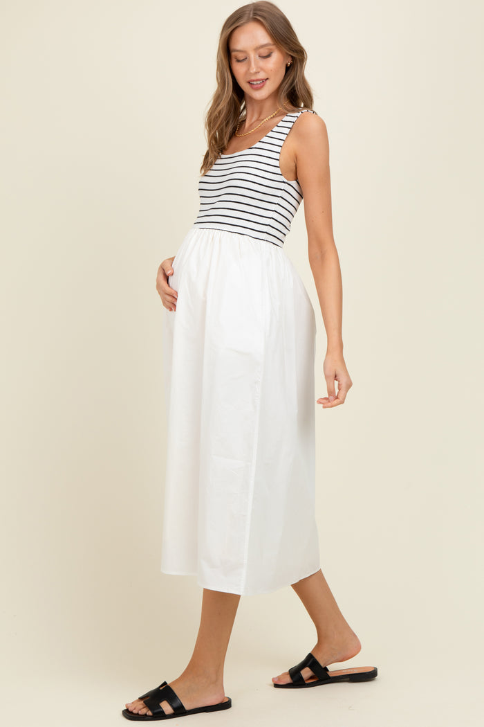 woman wearing a striped maternity tank top and a flowy white maternity midi skirt, gently holding her baby bump