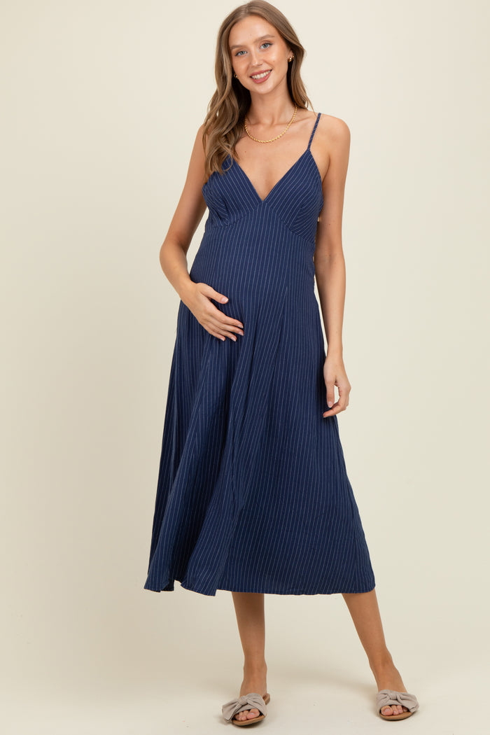 woman wearing a navy blue maternity dress with a v-neck and spaghetti straps, gently holding her baby bump