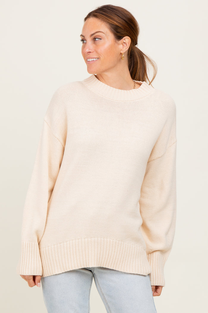 woman wearing a light beige oversized sweater with ribbed cuffs and hem, styled with light wash jeans