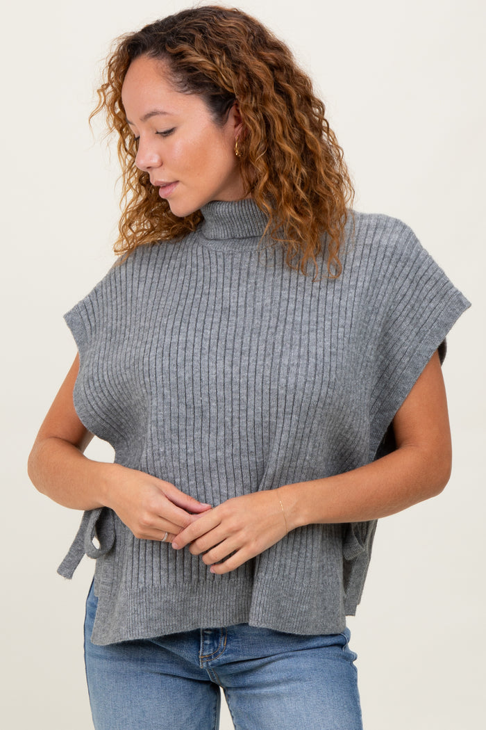woman wearing a gray ribbed knit poncho with a mock turtleneck and side ties, paired with blue jeans