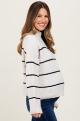 woman wearing a cream and black striped maternity sweater with a visible baby bump and dark jeans