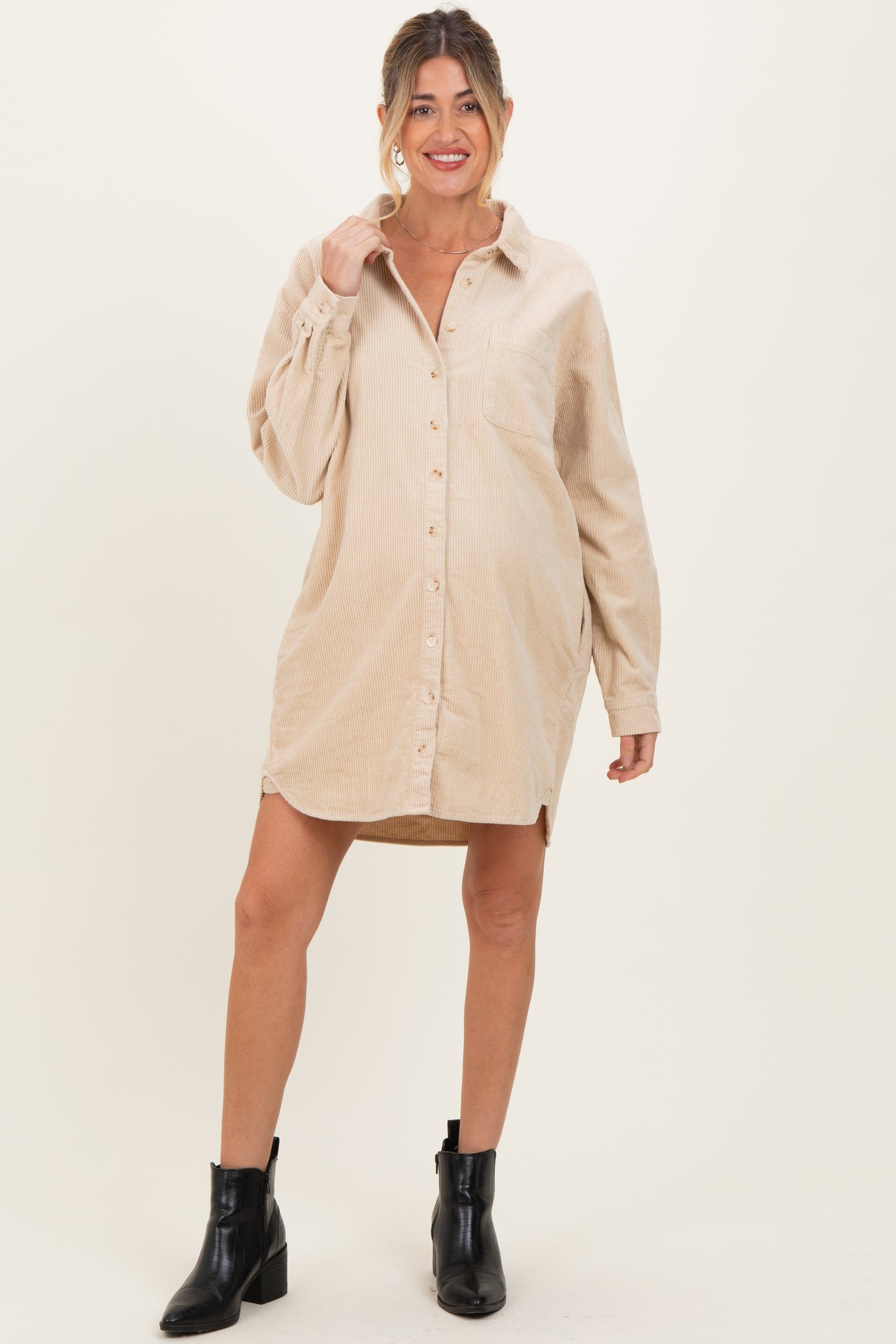 woman wearing a beige corduroy maternity shirt dress with buttons and long sleeves, smiling and standing confidently