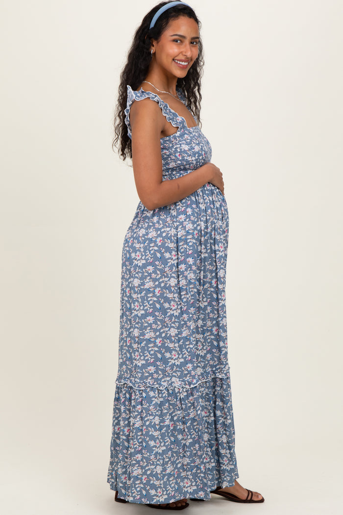 woman wearing a blue floral maternity maxi dress with ruffled straps and holding her baby bump