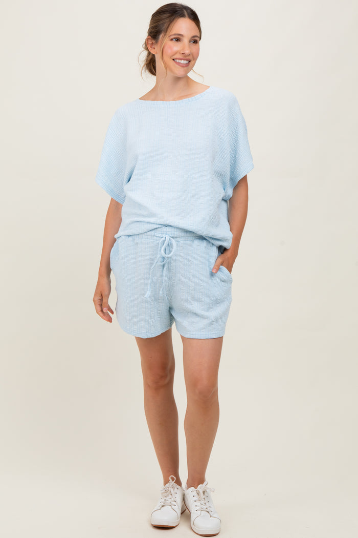 woman wearing a light blue maternity short set with a loose top and shorts, featuring pockets
