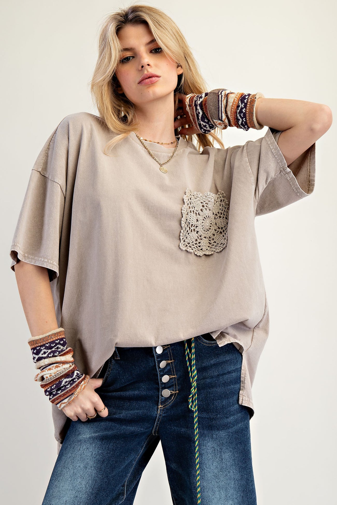 woman wearing a beige oversized t-shirt with crochet pocket and distressed jeans, accessorized with colorful knitted bracelets