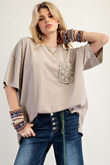 woman wearing a beige oversized t-shirt with crochet pocket and distressed jeans, accessorized with colorful knitted bracelets