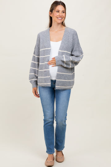 woman wearing a gray and white striped maternity cardigan and holding her baby bump with blue jeans and flats