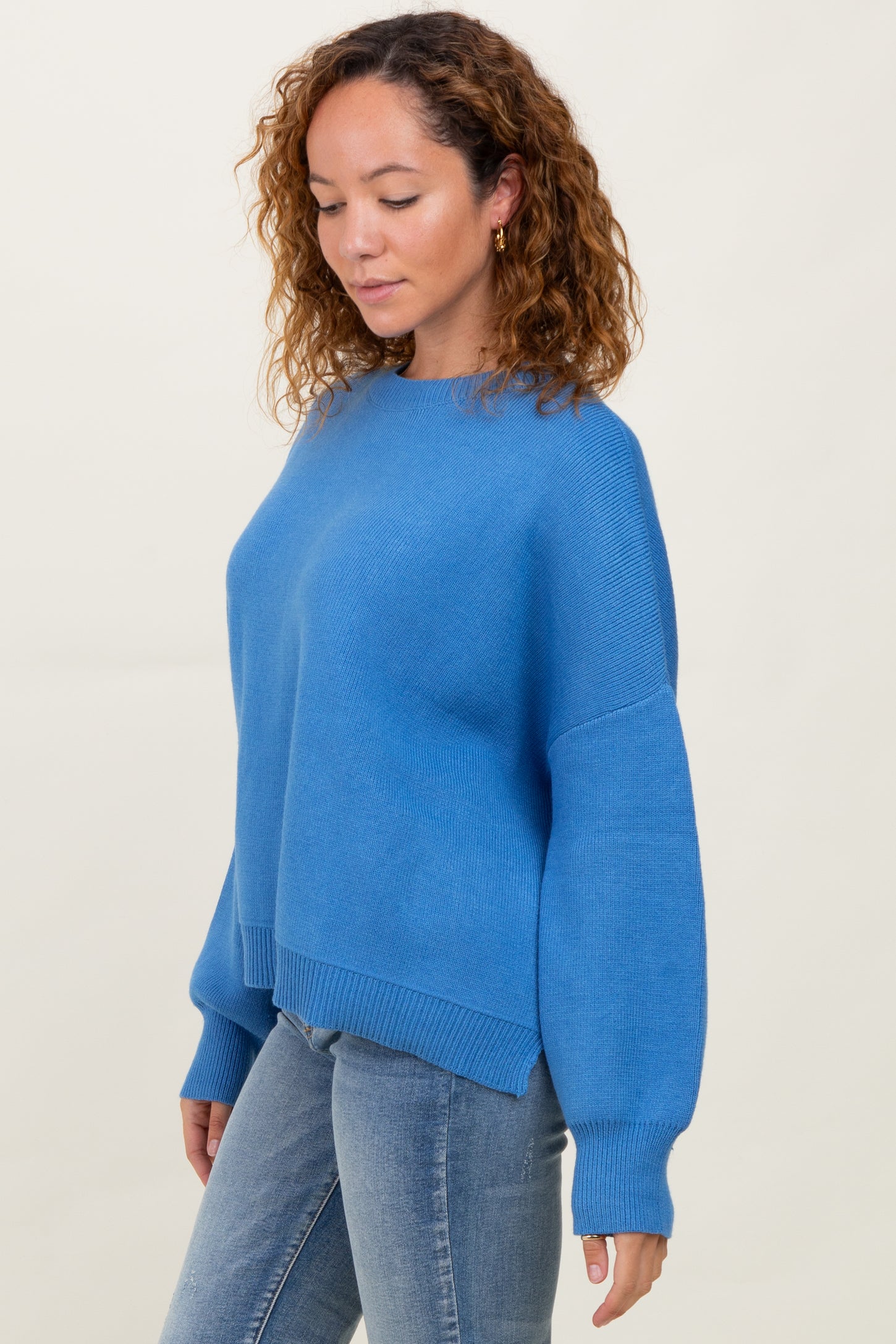 woman wearing a blue oversized sweater with long sleeves and a wide neckline, paired with light blue jeans