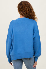 woman wearing a loose-fitting blue sweater with balloon sleeves and a ribbed hem, seen from the back