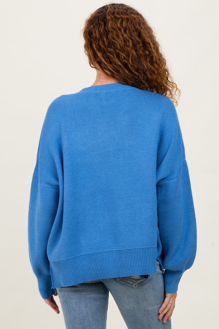 woman wearing a loose-fitting blue sweater with balloon sleeves and a ribbed hem, seen from the back