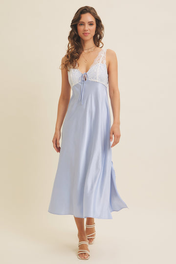 woman wearing a light blue satin slip dress with lace trim and adjustable tie detail, styled with strappy sandals