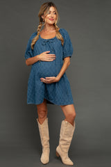 woman wearing a blue maternity dress with puffed sleeves and a drawstring, holding her baby bump and wearing knee-high tan boots