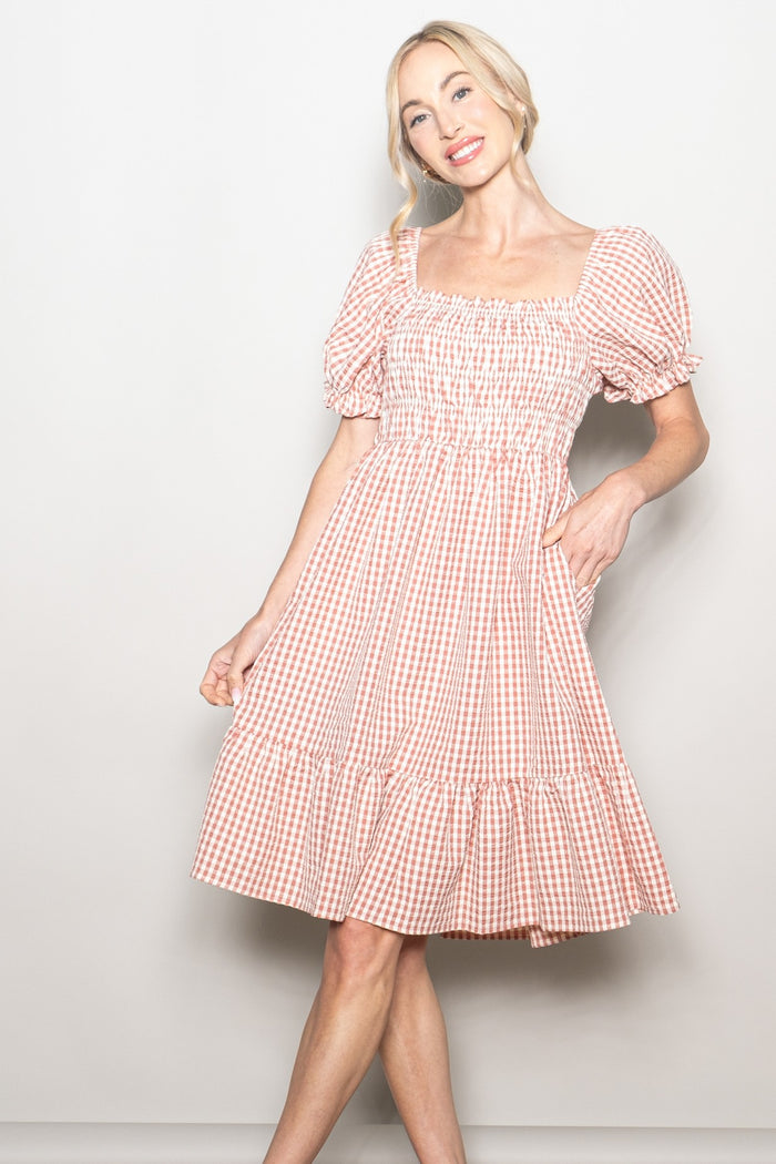 woman wearing a pink and white gingham puff sleeve dress with a smocked bodice and tiered skirt
