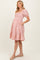woman wearing a pink and white gingham maternity dress with short puff sleeves and a tiered skirt, showing her baby bump