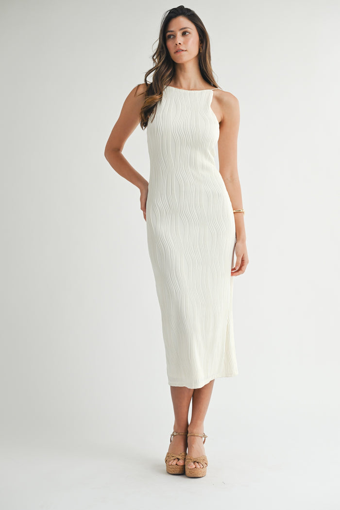 woman wearing a cream-colored ribbed midi dress with a halter neckline and a fitted silhouette