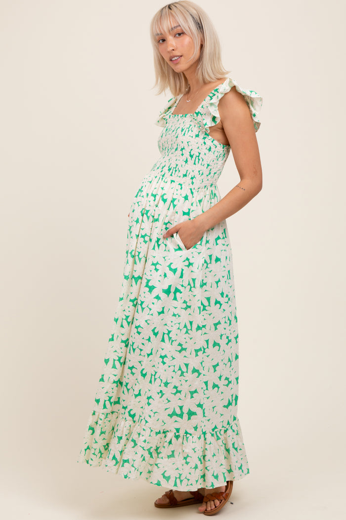 woman wearing a green and white floral maternity maxi dress with ruffle straps and pockets, showing off her baby bump