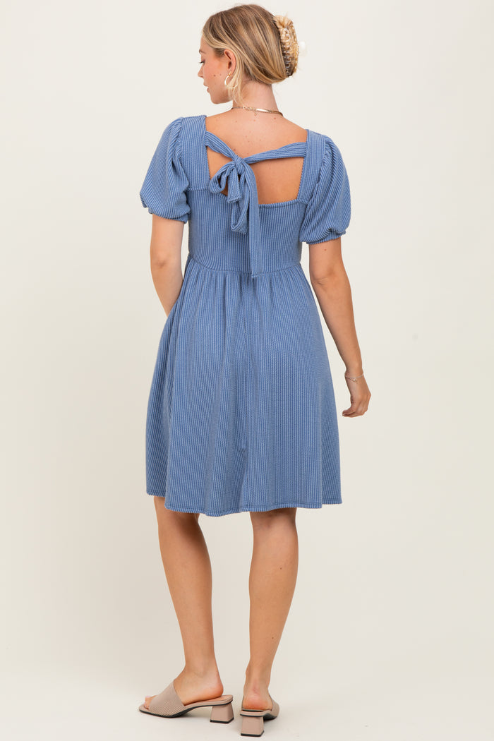 woman wearing a blue striped dress with puff sleeves and a tie-back detail, showing a fitted waist and flared skirt