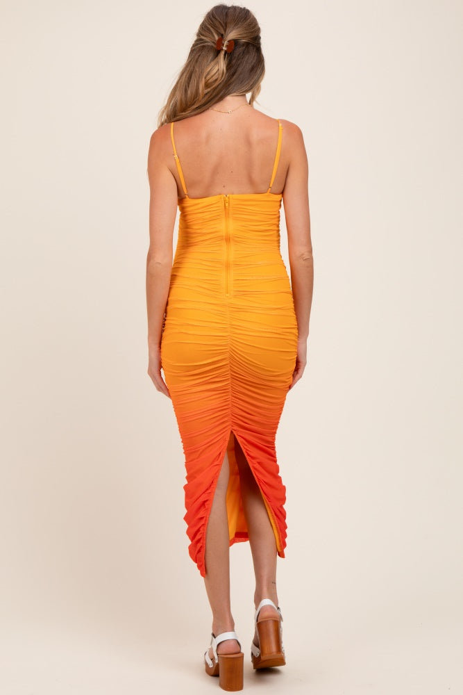 woman wearing a yellow to orange ombre maternity dress with ruched details and a back slit
