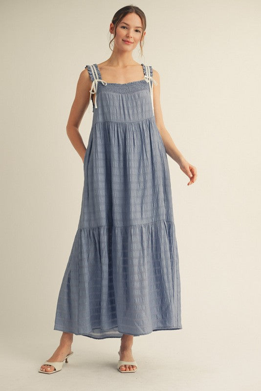 woman wearing a light blue maxi dress with adjustable shoulder straps and a tiered skirt