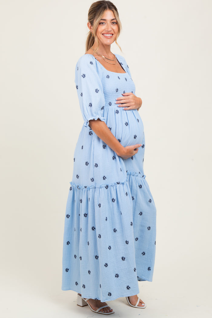 woman wearing a light blue maternity maxi dress with floral embroidery and a visible baby bump