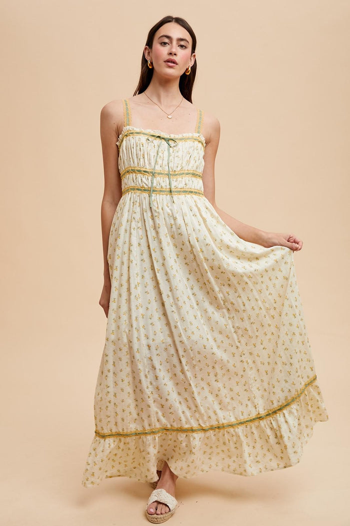 woman wearing a white floral maxi dress with yellow accents and adjustable straps, standing against a neutral background
