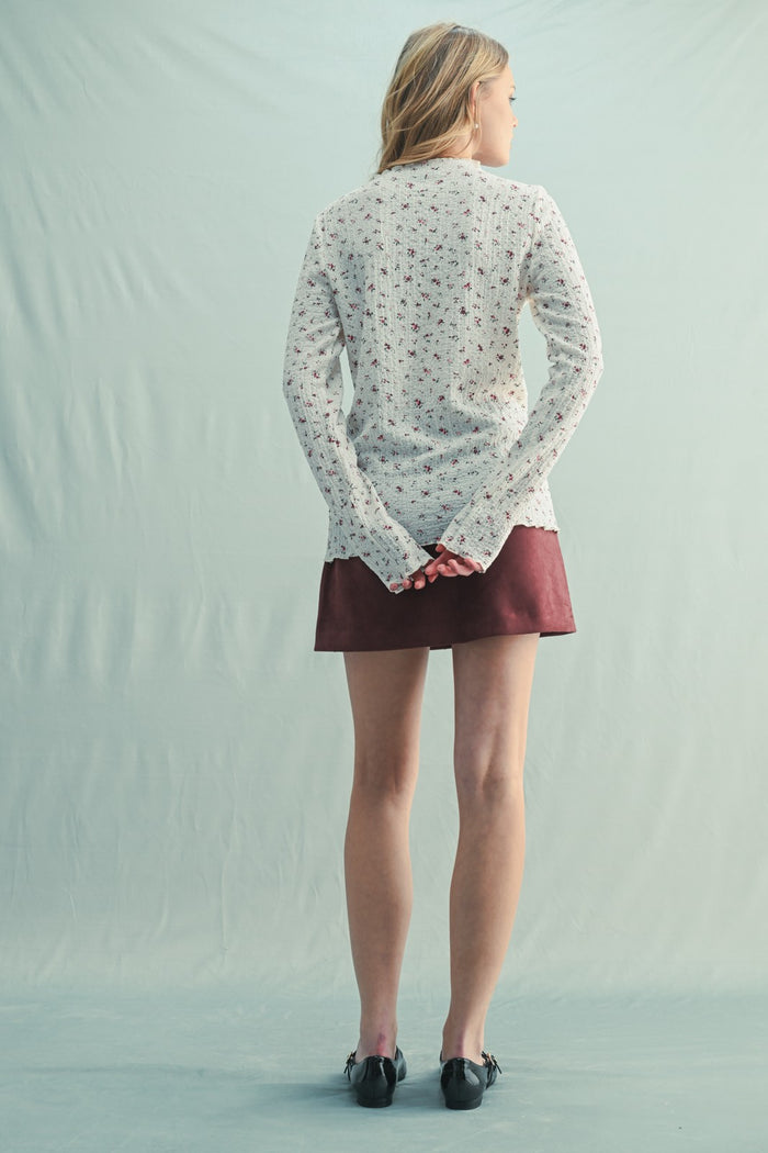 woman wearing a cream floral long sleeve sweater with a maroon skirt, viewed from the back