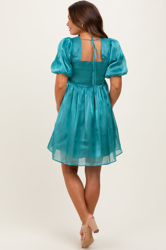 woman wearing a teal maternity dress with puff sleeves and smocked back, showcasing a flowy skirt