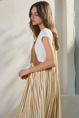 woman wearing a white short sleeve top under a tan striped pinafore dress, standing against a light background