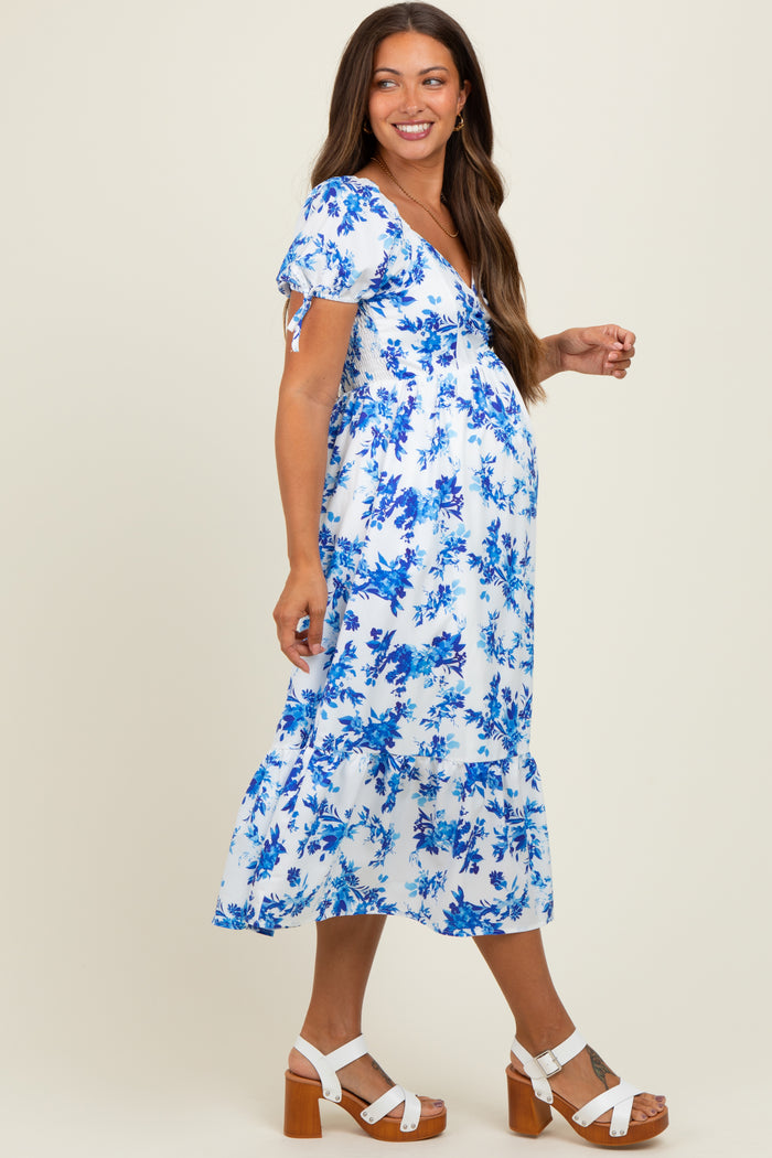 woman wearing a blue and white floral maternity dress with short sleeves and a tiered hem, showing her baby bump