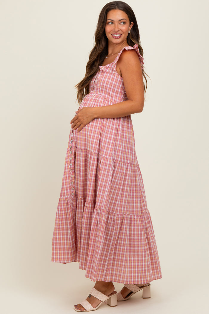 woman wearing a pink and white gingham maternity maxi dress with a tiered skirt and holding her baby bump