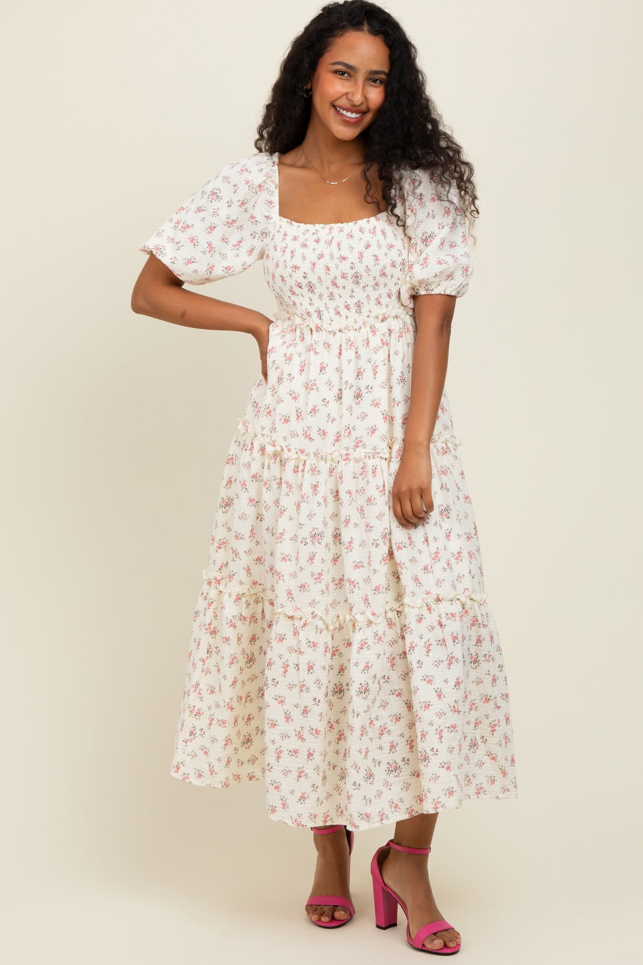 woman wearing a white puff sleeve floral maxi dress and pink heels, smiling against a neutral background