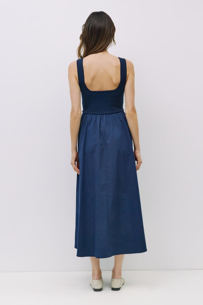 woman wearing a navy sleeveless maxi dress with a fitted bodice and a flared skirt, viewed from the back