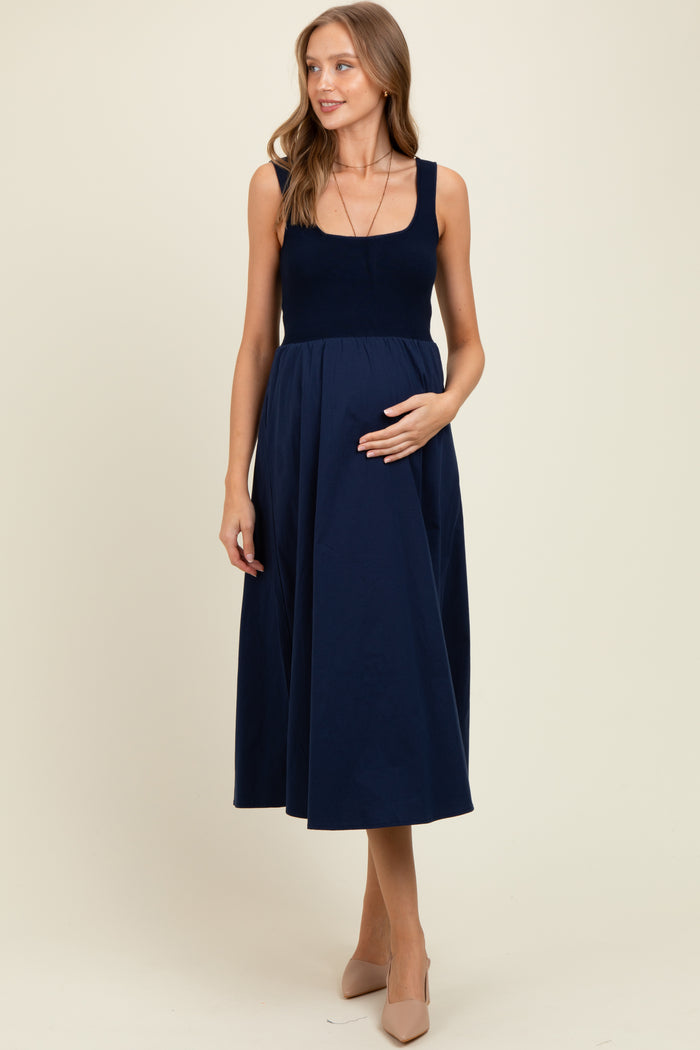 woman wearing a navy blue maternity dress with a fitted bodice and flowing skirt, holding her baby bump