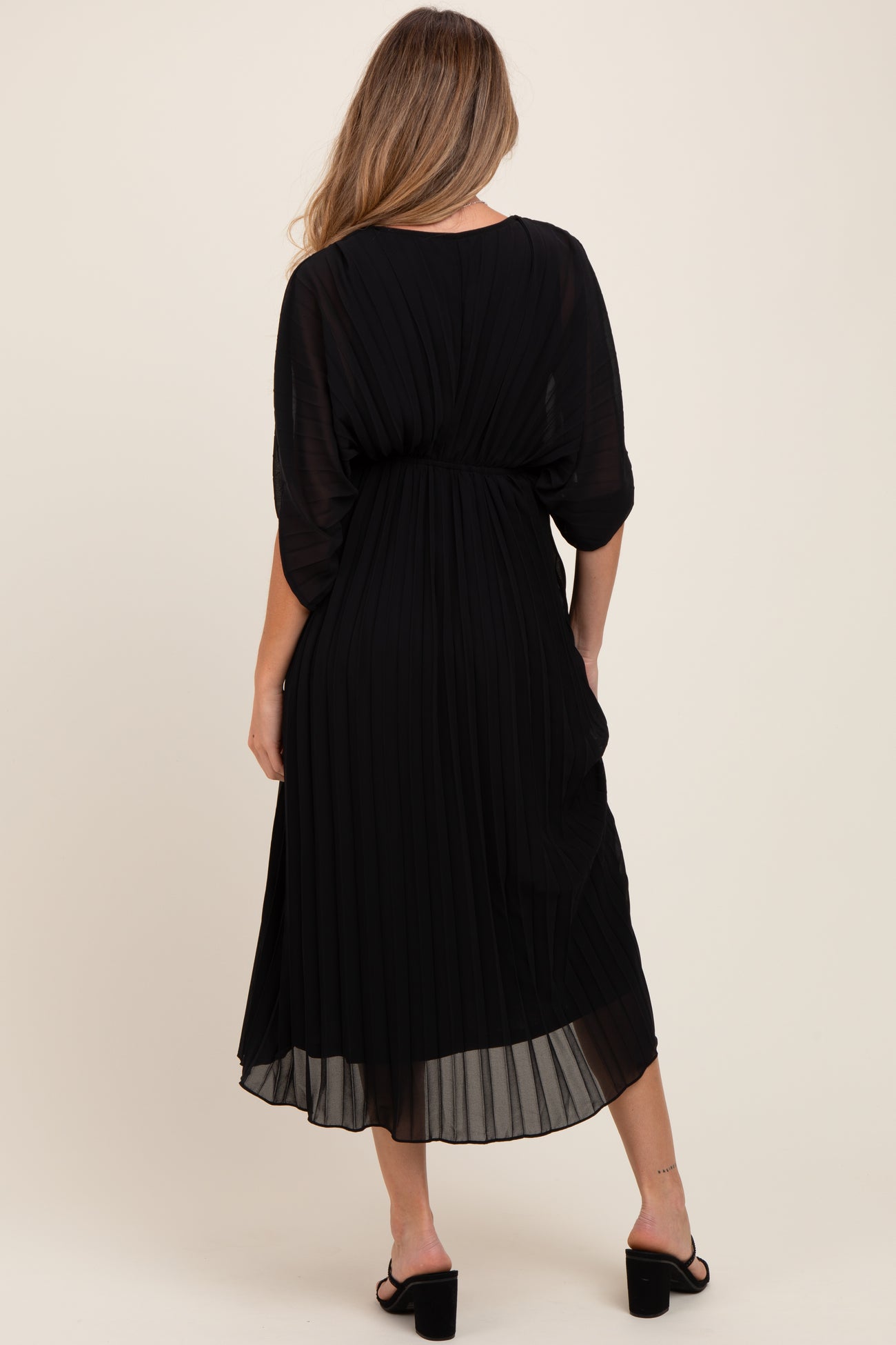 woman wearing a black pleated maternity dress with a flowing silhouette, showing a gathered waist and ankle length