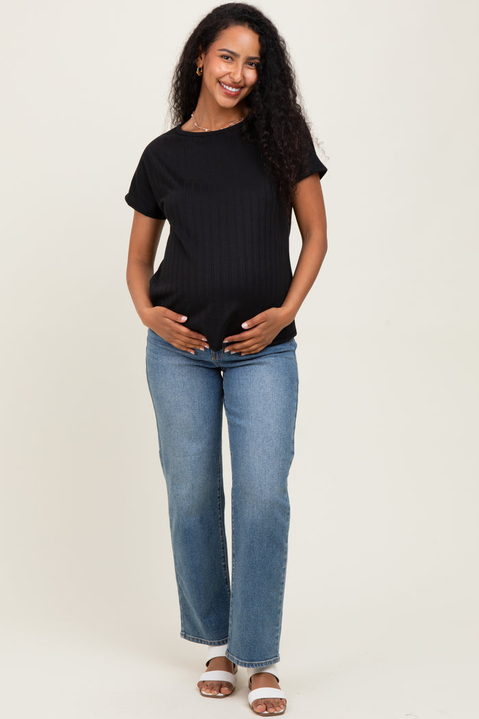 woman wearing a black ribbed maternity top and blue jeans, gently cradling her baby bump