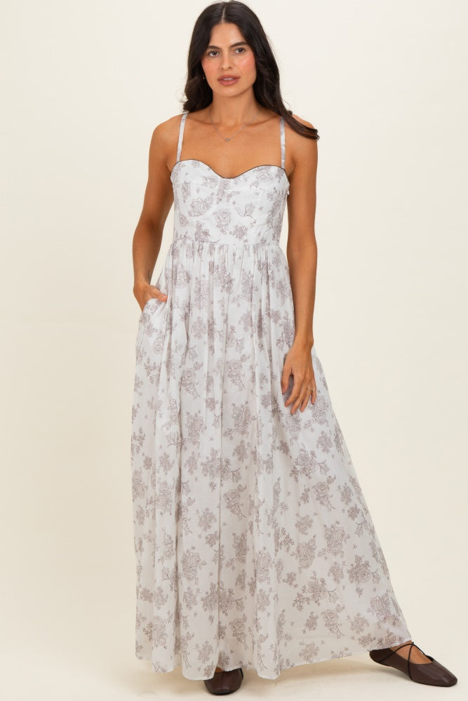 woman wearing a white floral maxi dress with a sweetheart neckline and spaghetti straps, standing with hands in pockets