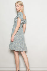 woman wearing a blue floral print short sleeve dress with a ruffled hem and an open back, posing sideways