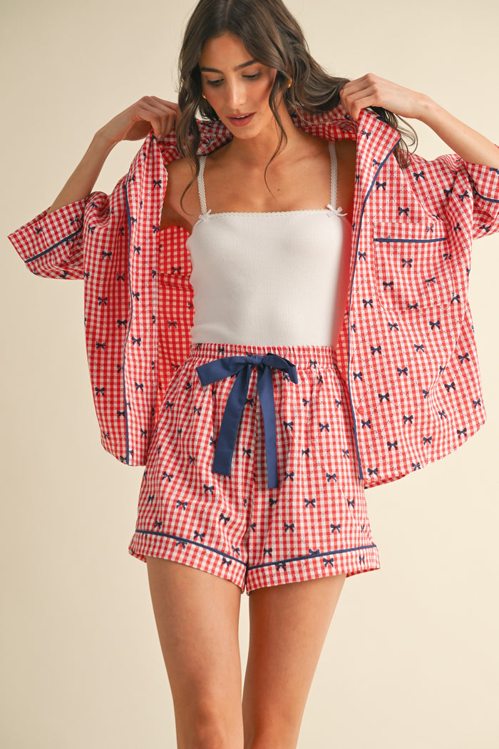 woman wearing a red and white gingham print pajama set with a short-sleeve button-up shirt and matching shorts