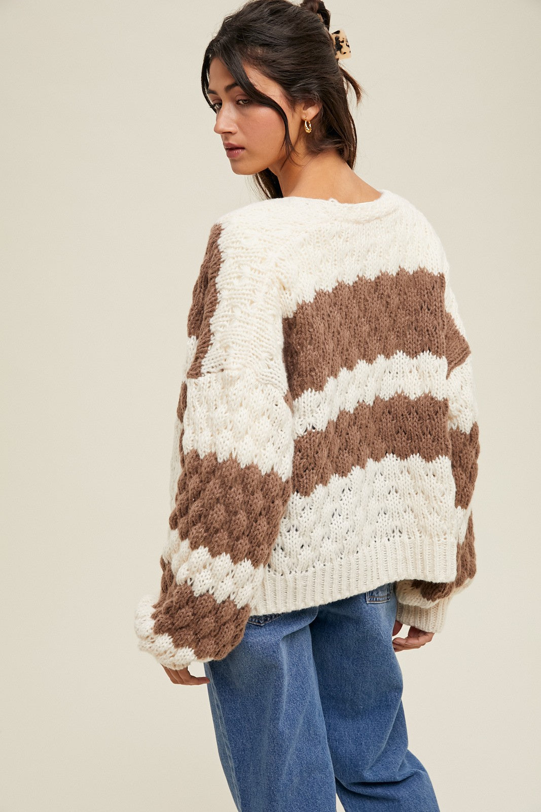 woman wearing a chunky knit sweater with brown and cream striped pattern, styled with high waisted jeans