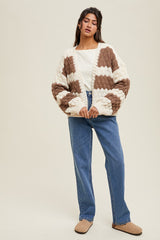 woman wearing a cream and brown color block chunky knit cardigan with a white top and blue high-waisted jeans
