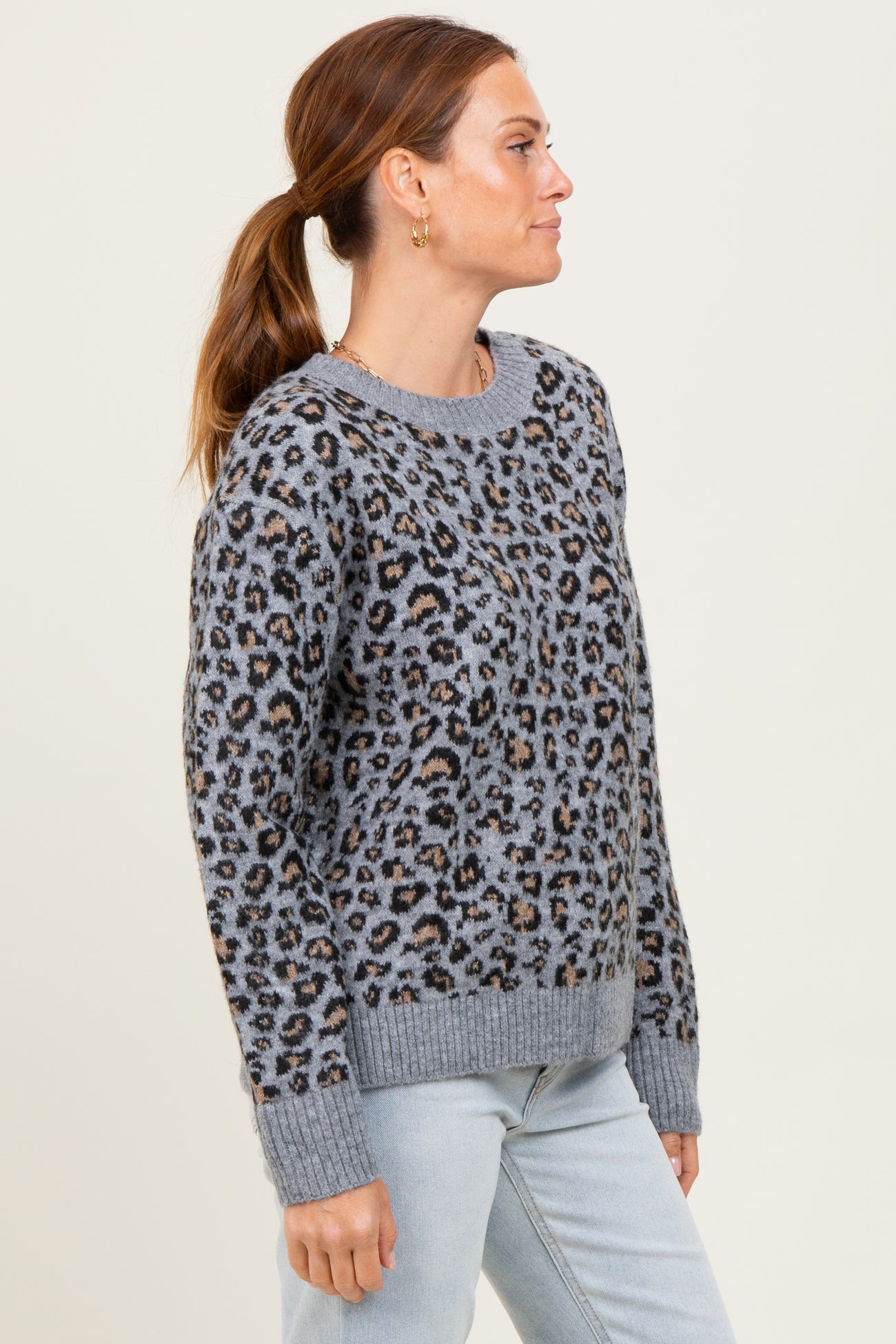 woman wearing a gray leopard print sweater with a relaxed fit and ribbed hem, styled with light blue jeans