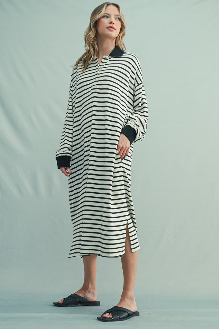 woman wearing a black and white striped long sleeve dress with side slits and black cuffs, standing in slides