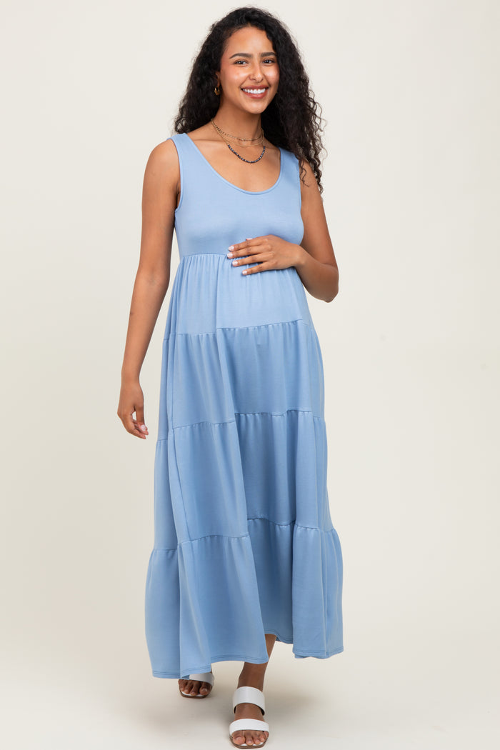 woman wearing a light blue sleeveless maternity maxi dress and holding her baby bump
