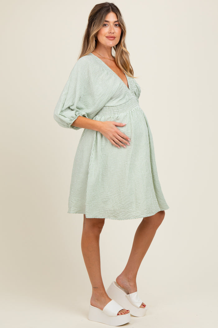 woman wearing a green and white striped maternity dress, gently holding her baby bump.