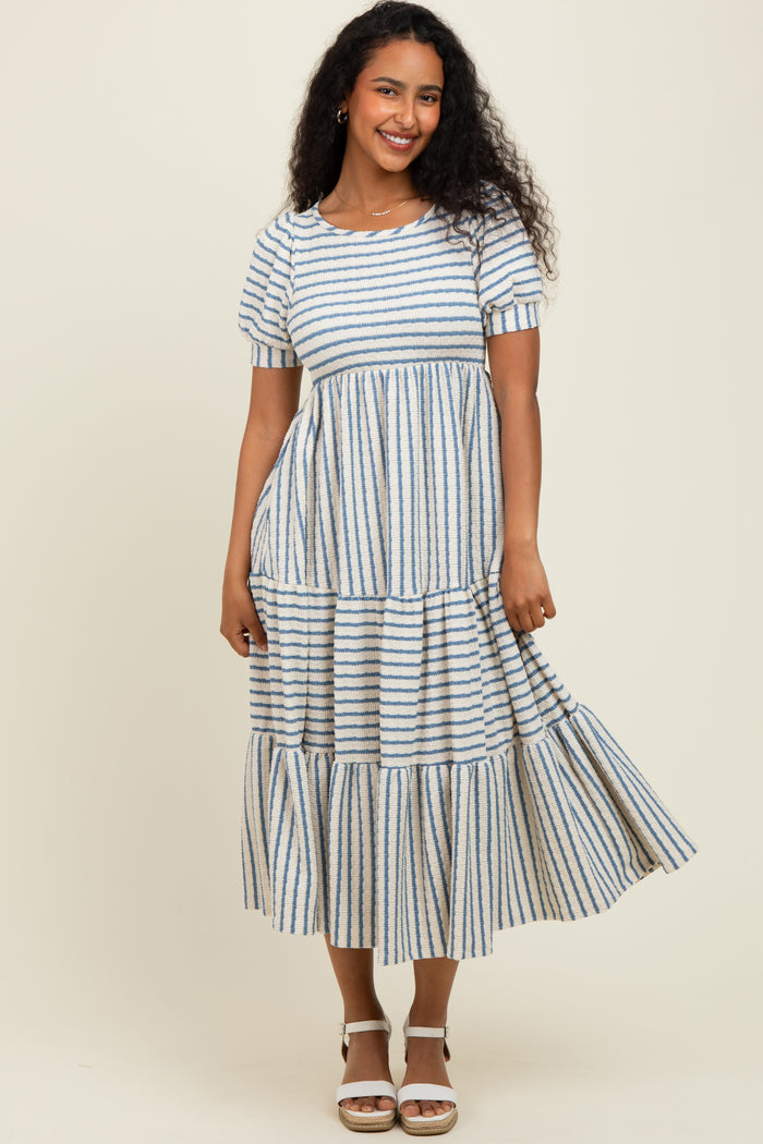 woman wearing a blue and white striped tiered midi dress with short sleeves and a rounded neckline